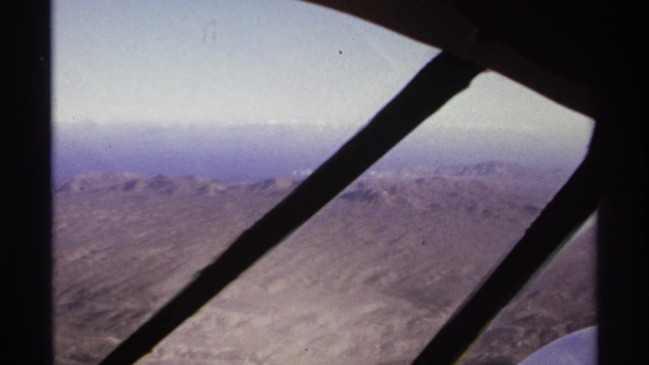 Mountain range seen through aircraft window braces with a distant hazy horizon.