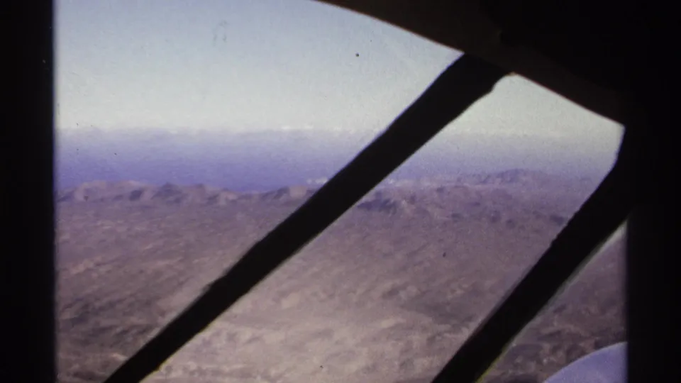 Aerial view from inside a plane near La Paz, Mexico, showing rocky desert mountains through dark diagonal window braces.