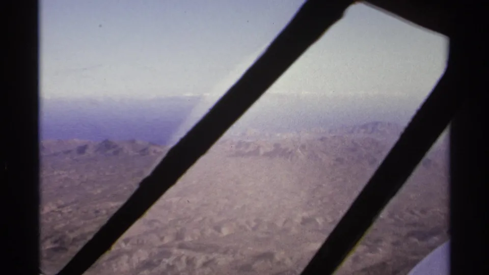 A plane-window view near La Paz, Mexico, with diagonal supports crossing a hazy aerial view of arid mountain terrain.