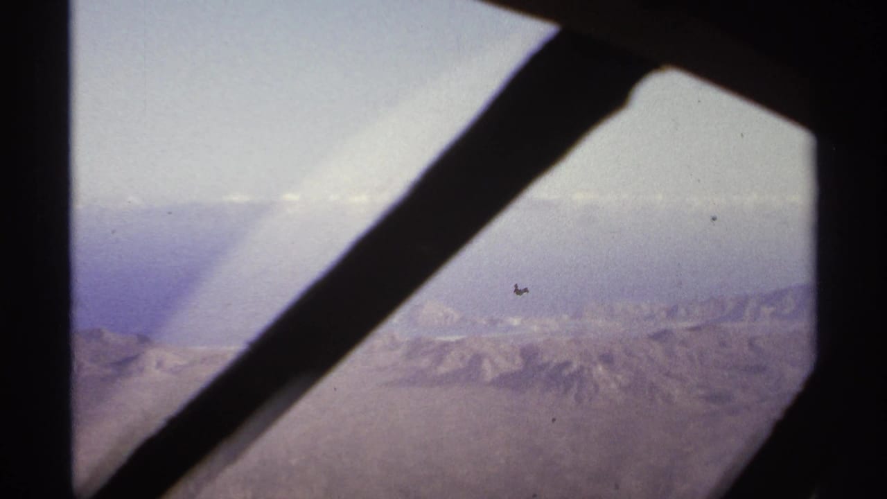 Dark window struts cross a hazy aerial view of distant mountain ridges.