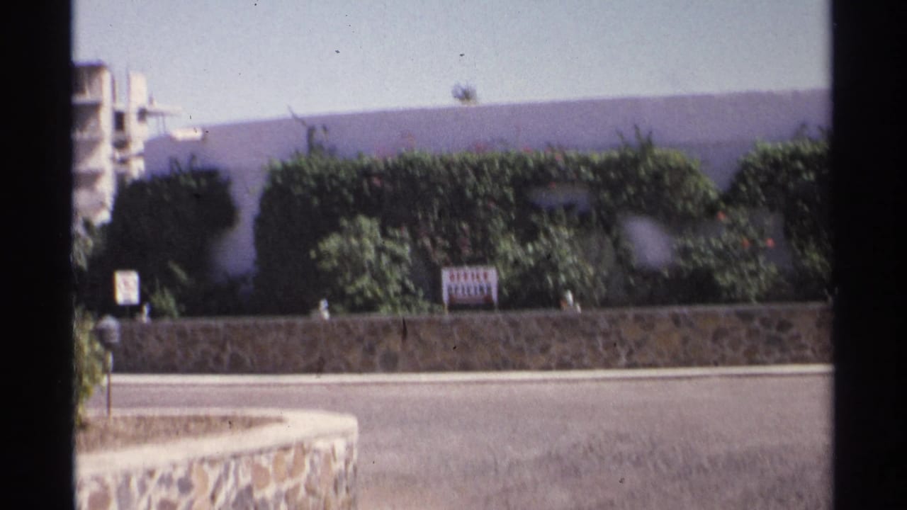 Street view with stone wall, hedges, office sign, and concrete building behind it.