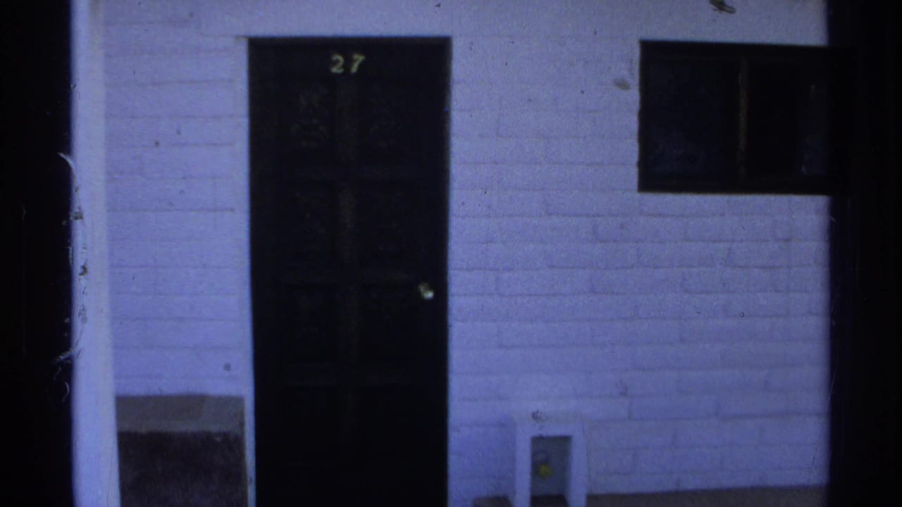 Dark apartment door marked 27 beside a small window and white exterior wall.