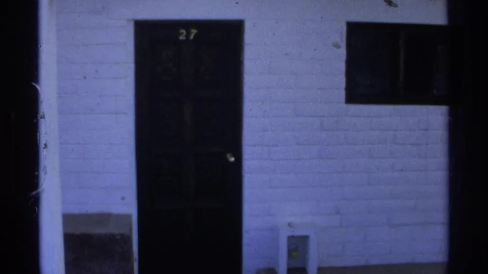 1975 Guaymas home-movie frame showing apartment door 27, a small window, columns, and white exterior wall.