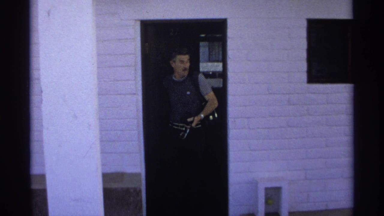 Adult man exits an apartment doorway in Guaymas, Mexico, holding a camera or small filming device in a 1975 8mm frame.