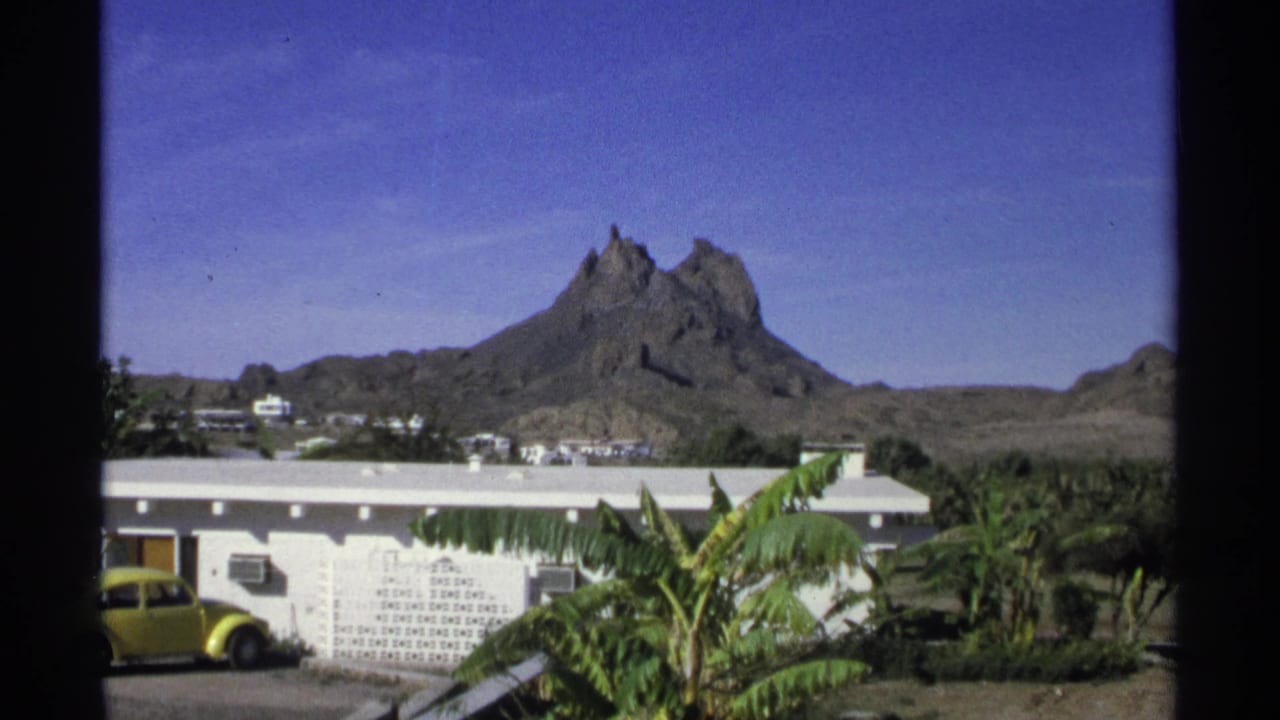 A wide Guaymas view shows a distinctive rocky mountain above low buildings, palm foliage, and a yellow vintage car.