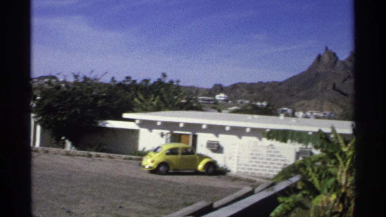 White low-rise building with a yellow car parked outside and a rocky mountain in the background.