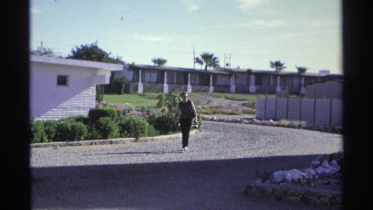 Man walking on a gravel path outside low white hotel buildings with palm trees.