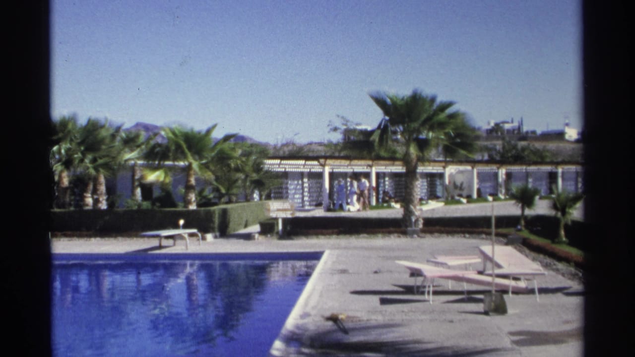 1975 resort pool area in Guaymas with lounge chairs, palms, cabana-like structures, and small groups of people in the distance.
