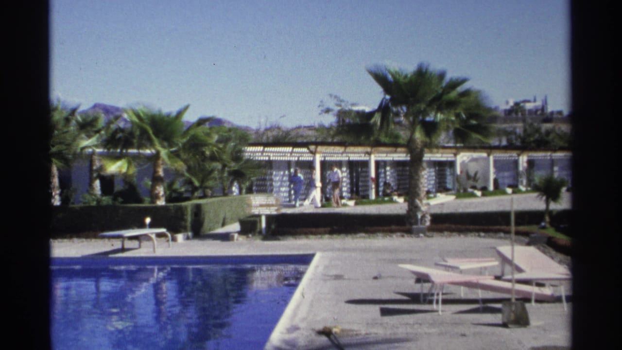 Guaymas resort poolside scene from 1975 with blue water, empty loungers, palms, and distant guests near the hotel structure.
