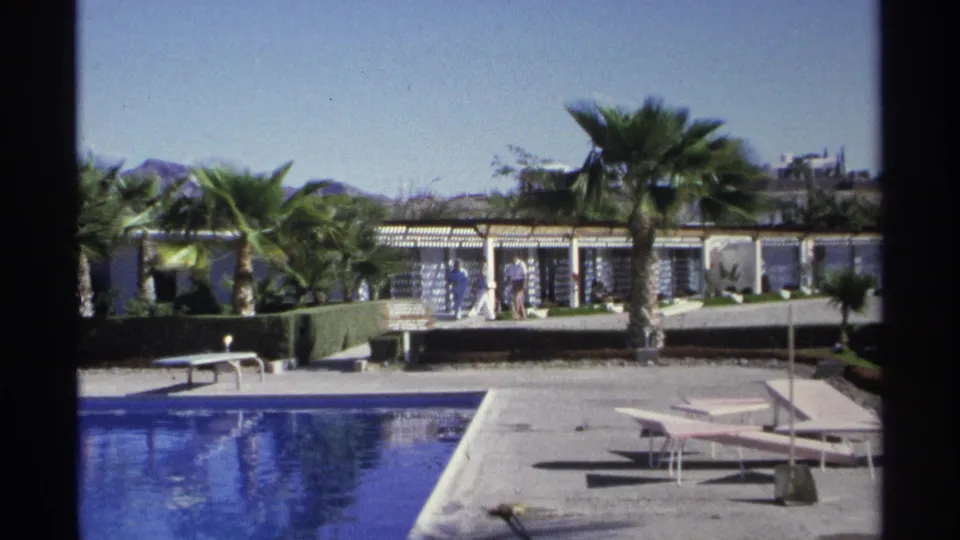 Guaymas resort poolside scene from 1975 with blue water, empty loungers, palms, and distant guests near the hotel structure.