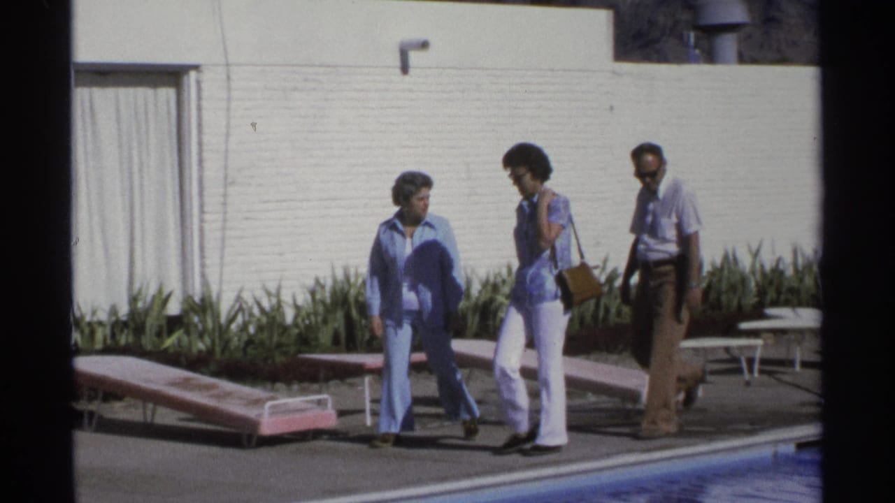 Three adults move along the poolside near pink lounge chairs, a white wall, plants, and a curtained doorway in Guaymas home-movie footage.