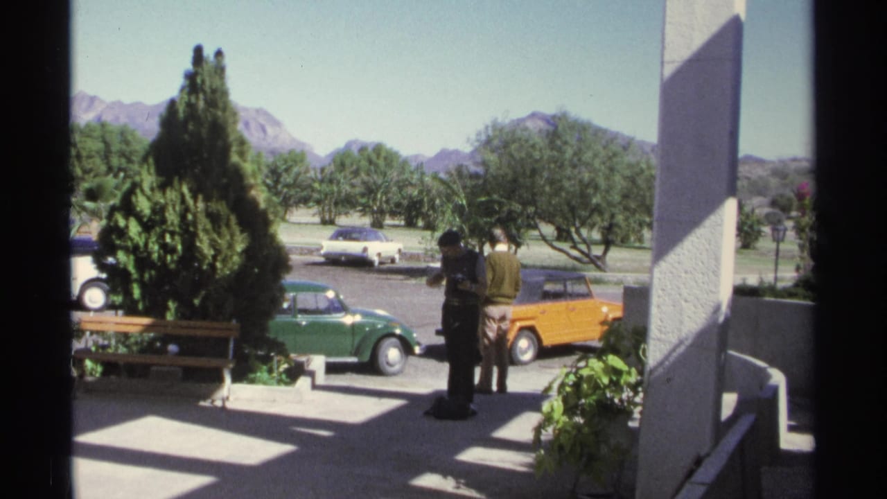 A Guaymas parking lot shows classic cars, including a green Beetle-style car and an orange vehicle, with trees and mountains beyond.