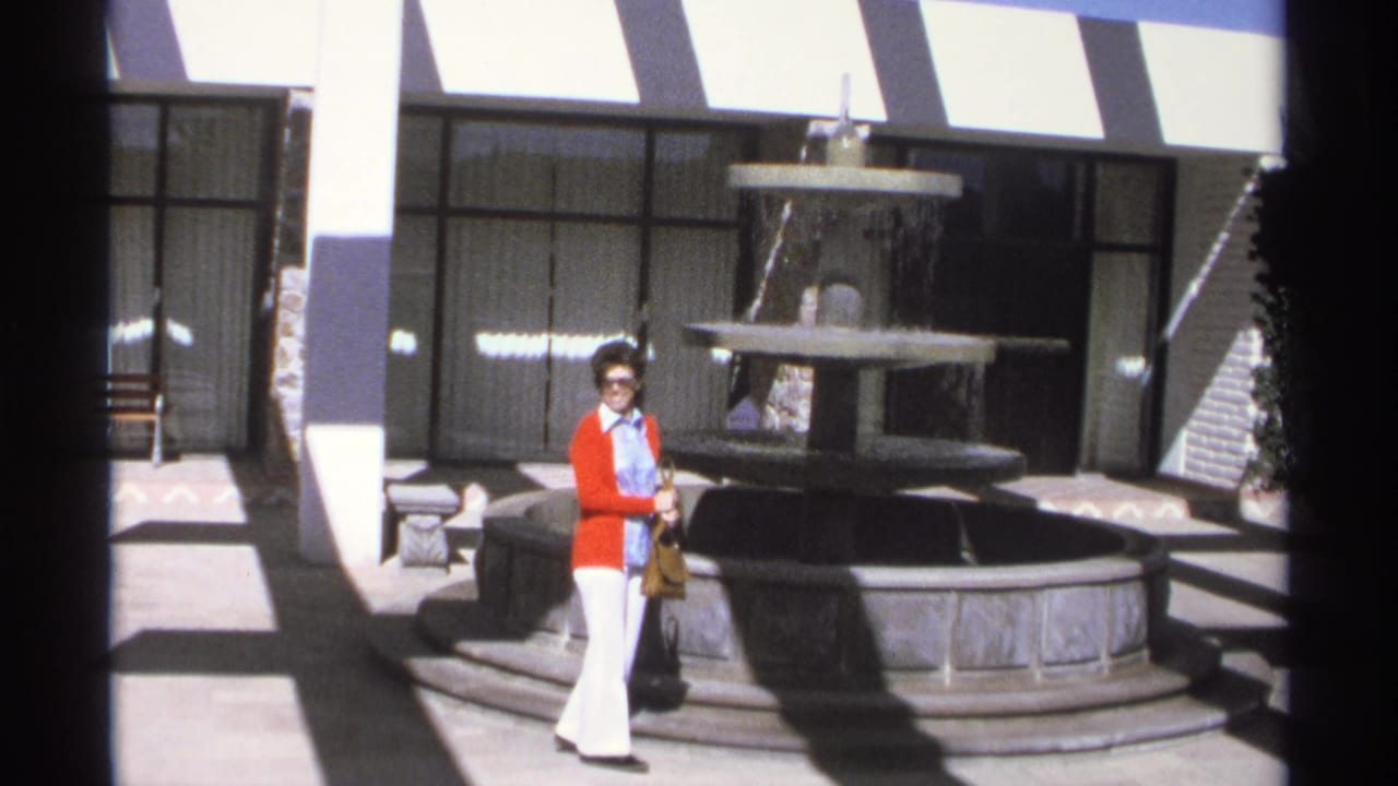 Woman standing near the fountain with striped awning and dark glass doors behind her.
