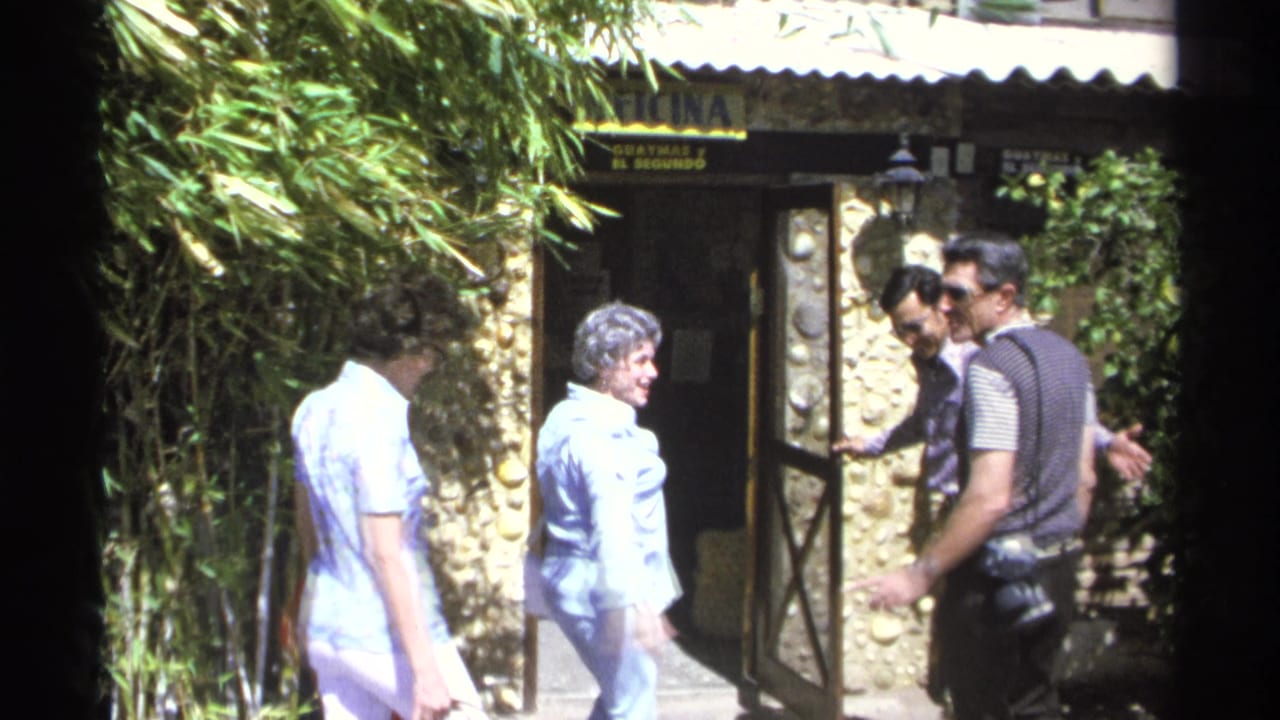Adults walk toward a stone-walled entrance beneath Spanish signage and leafy plants.