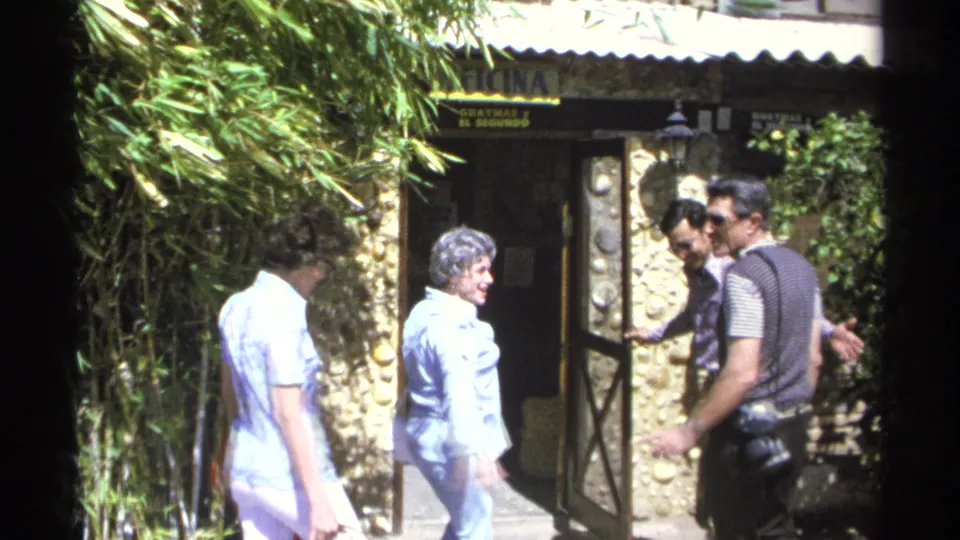In Guaymas, Mexico in 1975, adults in casual 1970s clothing approach a doorway with signage and bamboo nearby.