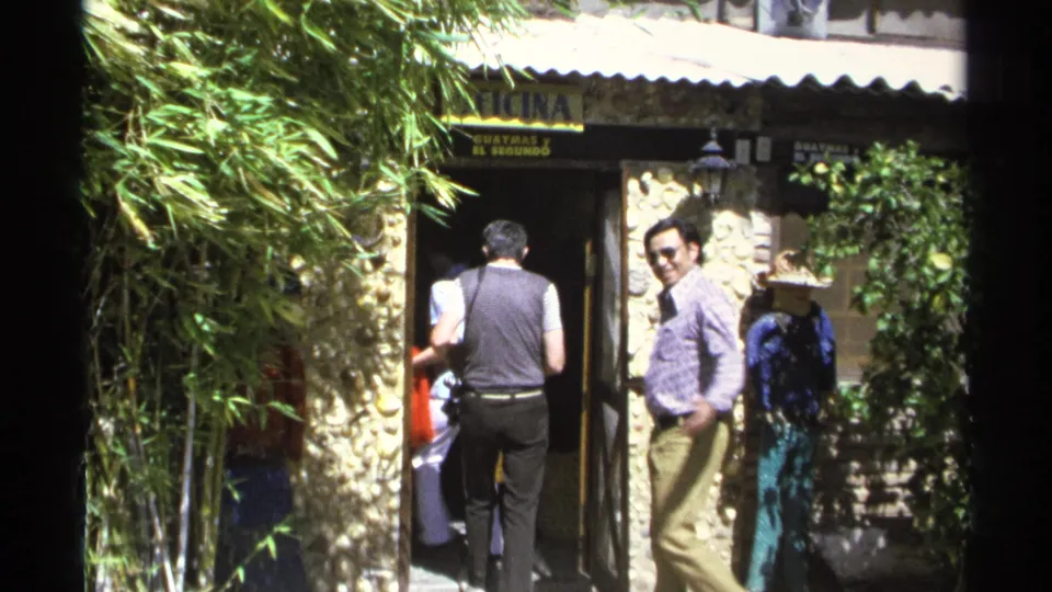 At the end of the Guaymas 1975 clip, most adults enter while a man in sunglasses turns back beside the stone wall.
