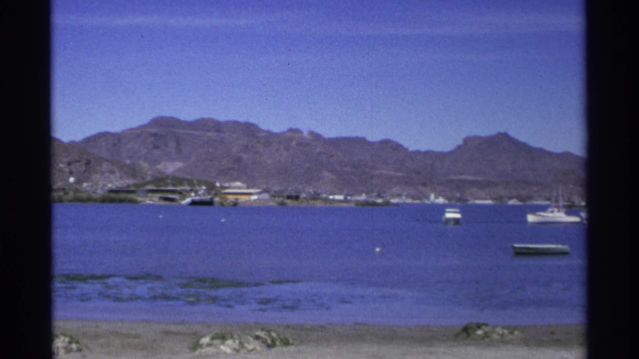 Wide harbor view with anchored boats, distant shore and mountain range.