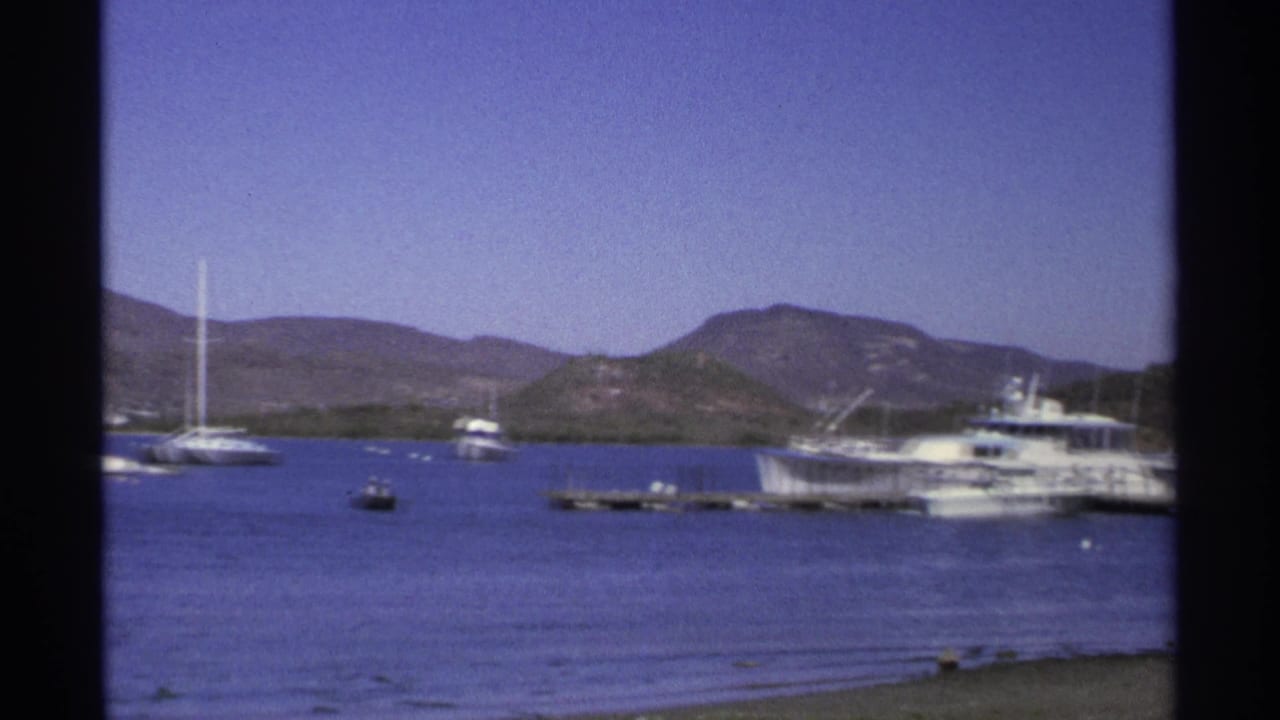 1975 Guaymas marina view with white motor yachts, small boats, calm bay water, and low hills beyond the shoreline.