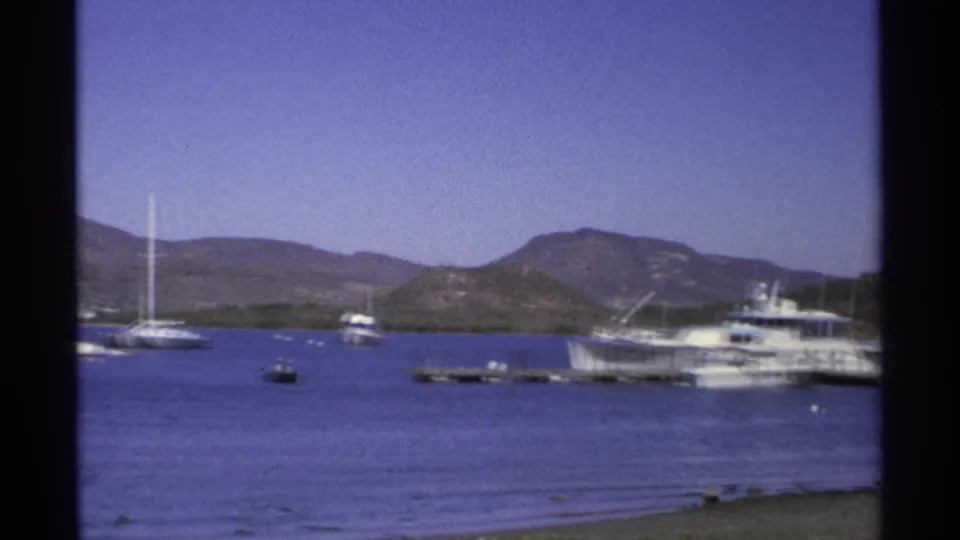1975 Guaymas marina view with white motor yachts, small boats, calm bay water, and low hills beyond the shoreline.