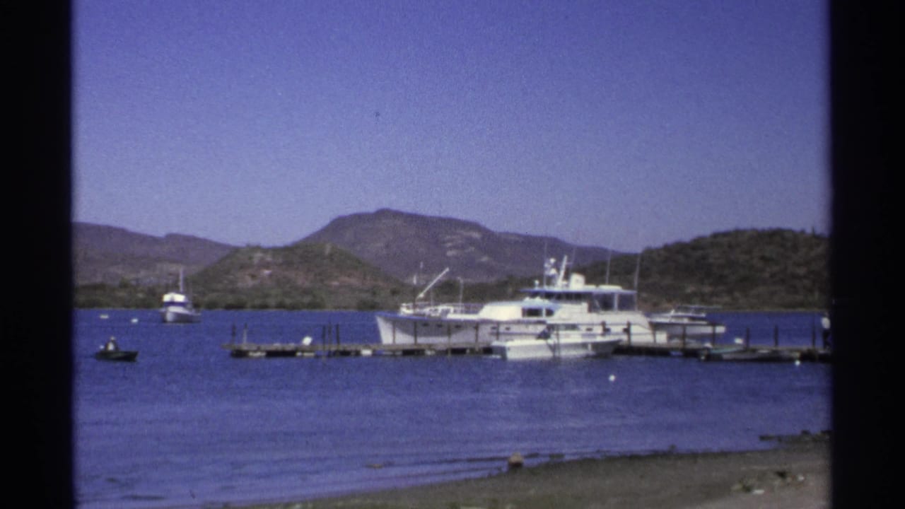 Motor yachts moored beside docks on calm water with hills behind.