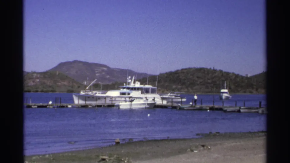 Guaymas marina footage shows a white motor yacht beside docks, small visible people on the pier, calm water, and hills in the distance.