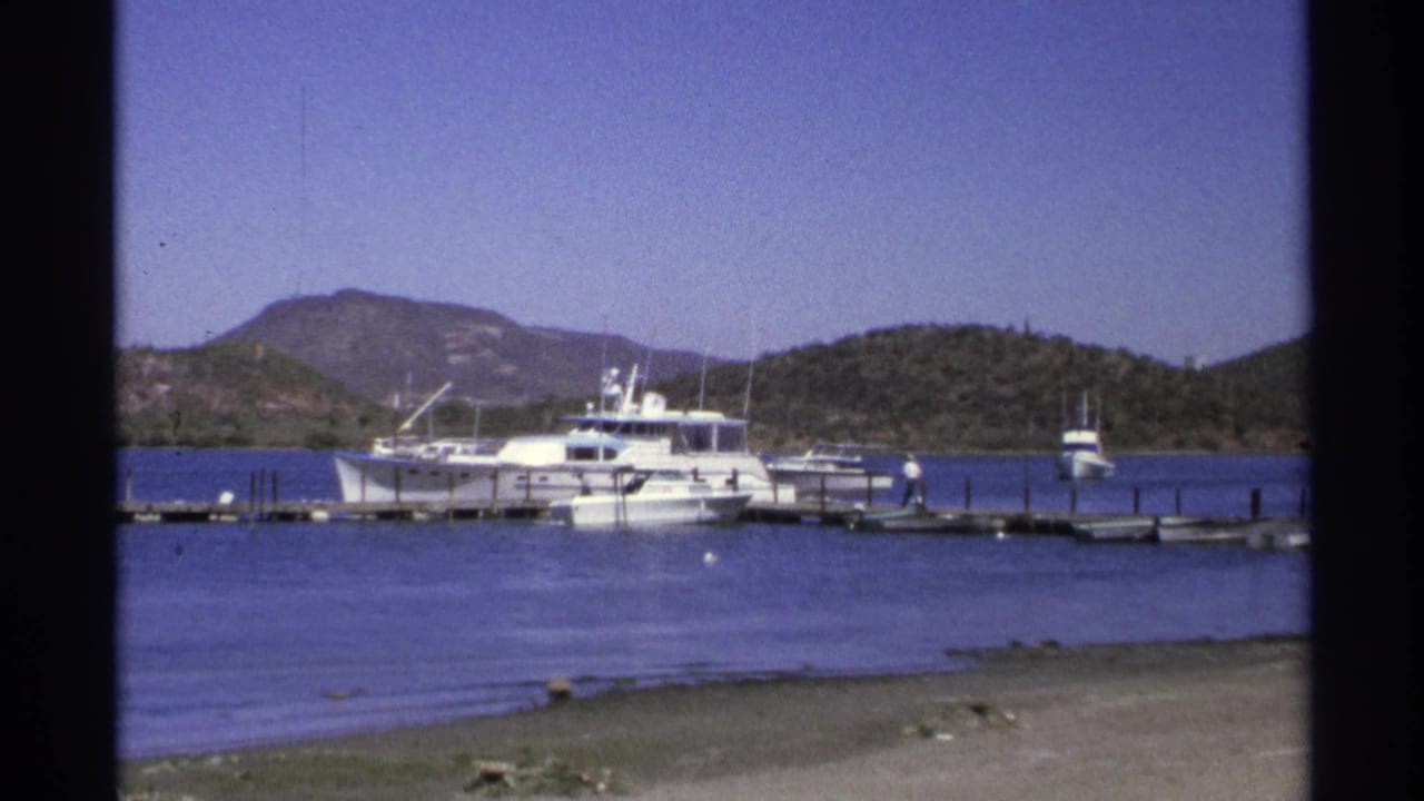 Guaymas, Mexico marina view from 1975 8mm footage, with white boats at wooden docks and low hills in the background.