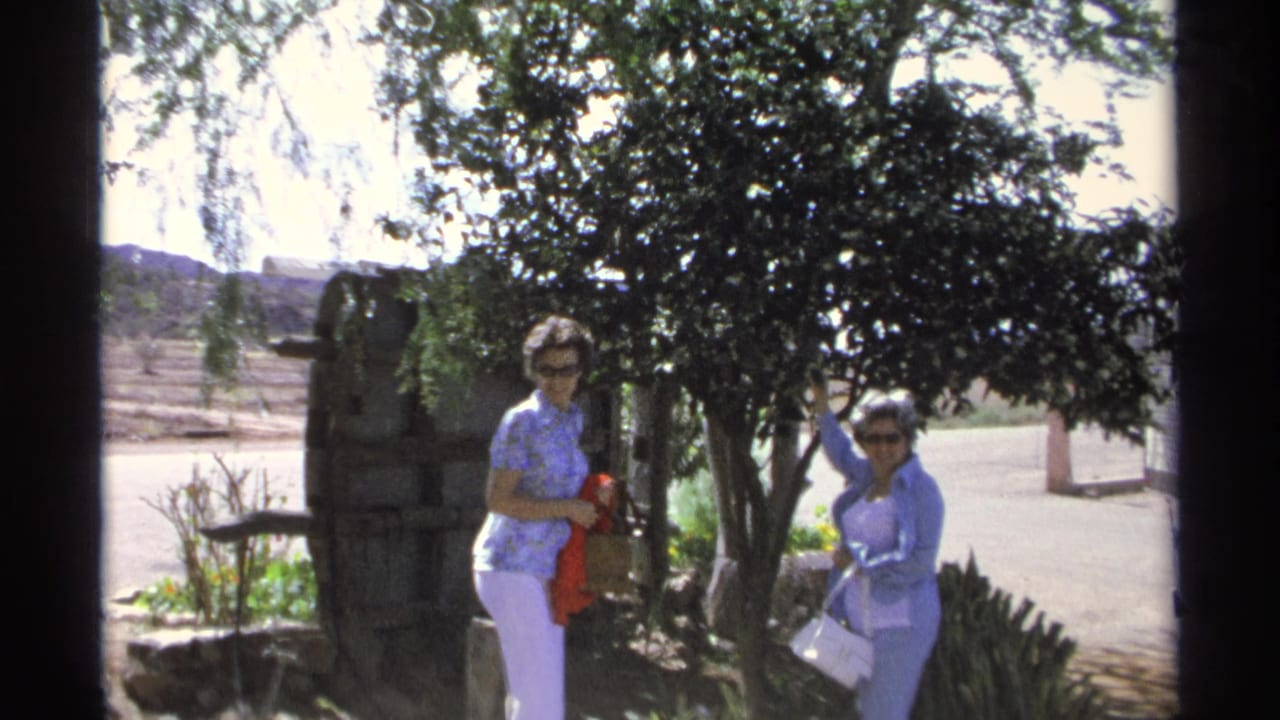 In 1975 Guaymas, Mexico footage, two women stand near a leafy tree as one holds a red scarf and the other faces the camera.