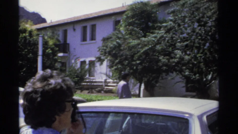 The camera widens to show a residence, a parked car, trees, and people in the Guaymas home-movie scene.
