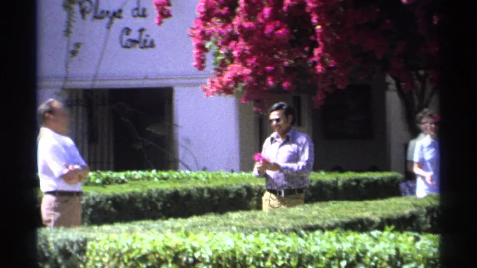 Adults stand in a landscaped Guaymas garden with partial Playa de Cortés lettering visible on the white building behind them.