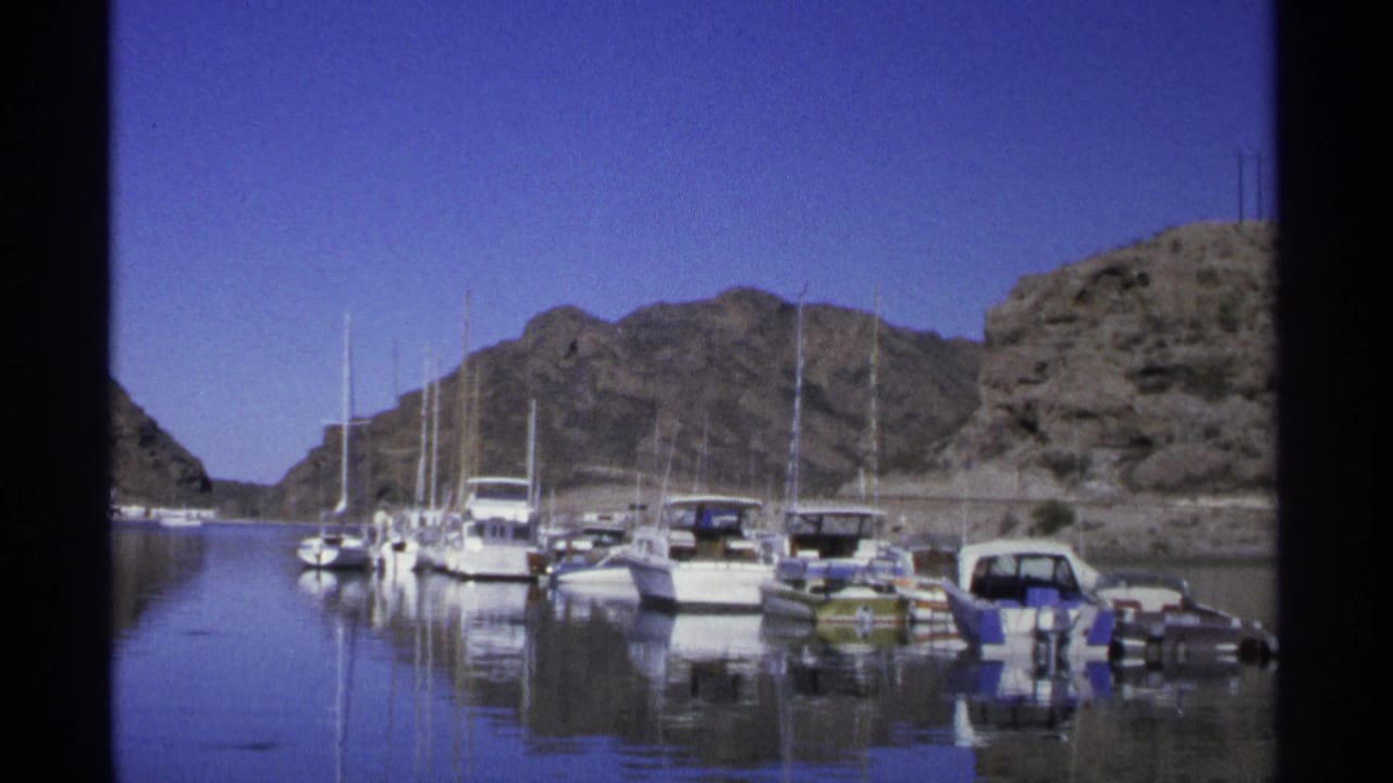 Boats moored in calm marina water with rocky hills behind them.