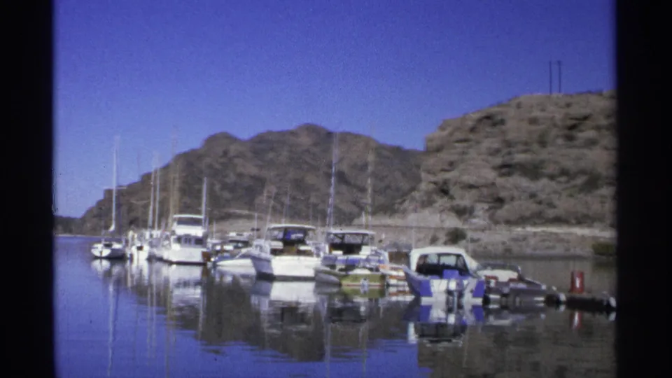 Wide 8mm view of a Guaymas marina, showing clustered boats, still reflections, a rocky shoreline, and clear blue sky.