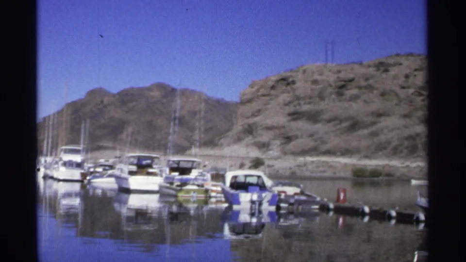 Guaymas, Mexico marina frame from 1975 with moored boats, floating markers, reflective water, and rocky hills in the background.