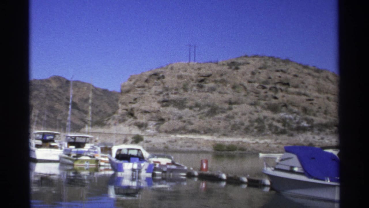 Moored boats and a blue-covered motorboat beside a rocky marina shore.