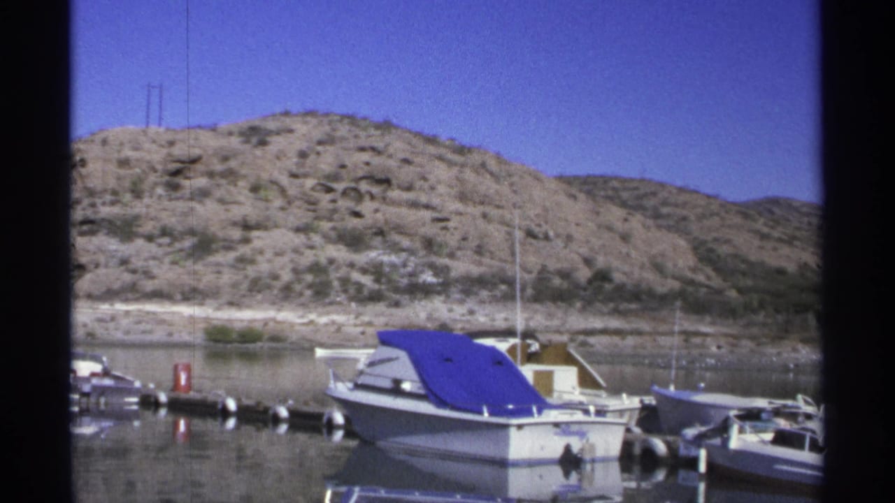 Small boats moored at a marina with arid hills behind them.