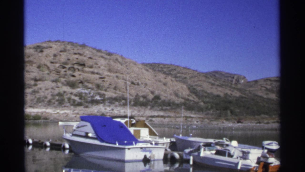 Motorboats tied near a dock with rocky hills across calm water.