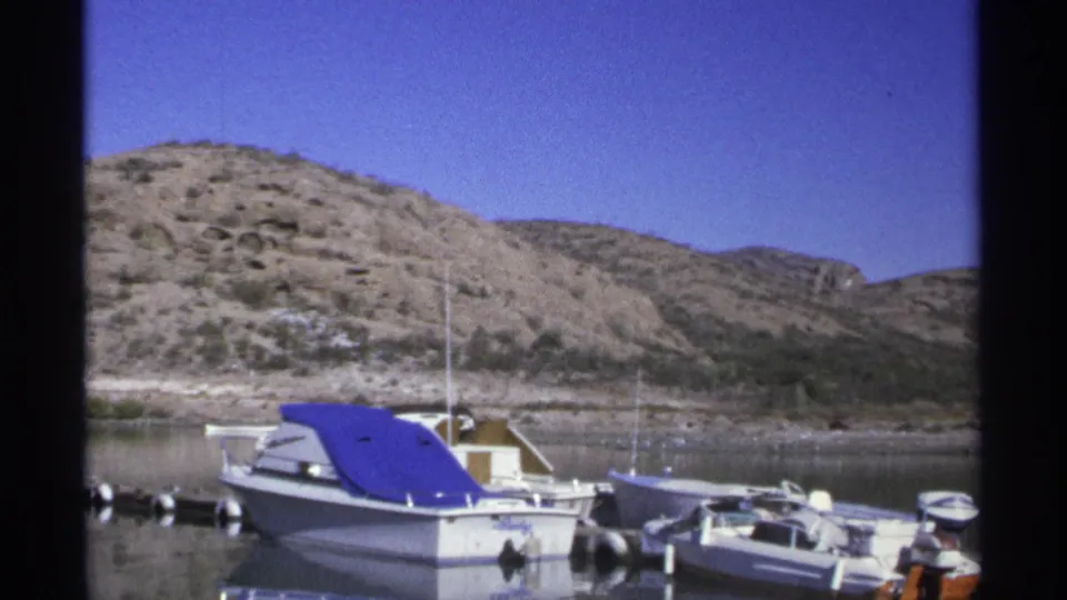 Guaymas, Mexico marina scene from 1975 showing moored boats, a bright blue cover, reflective water, and dry hills.