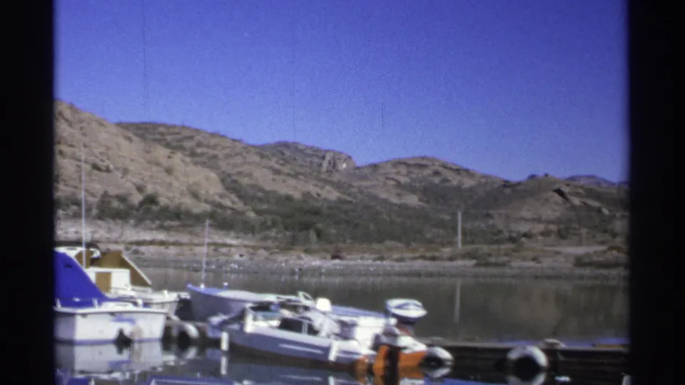 Guaymas marina footage from 1975 showing docked motorboats, a blue boat cover, calm water, and rocky desert-like hills.