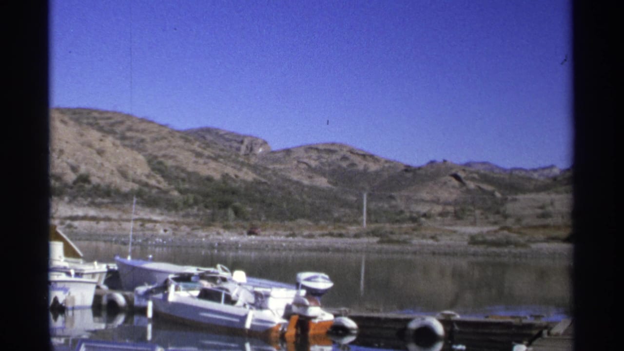 Small boats moored at a dock on calm water with rocky hills behind.