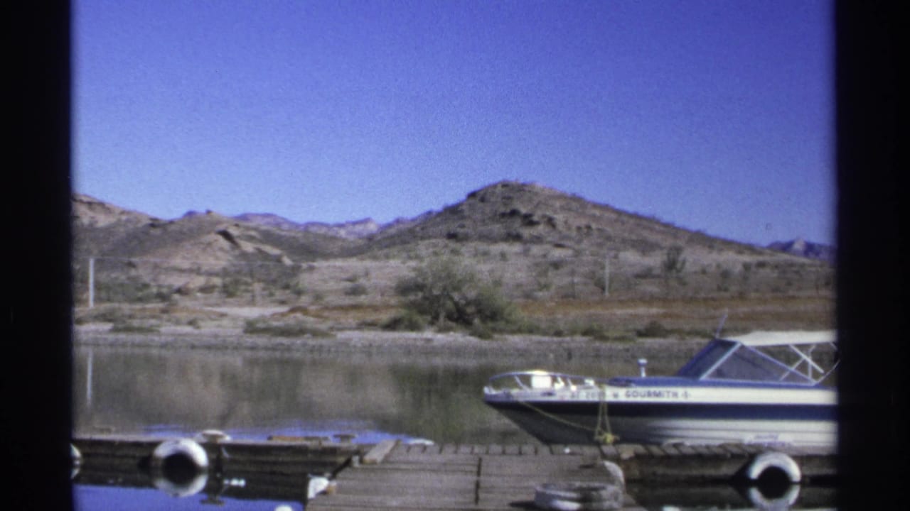 White and blue motorboat tied at a wooden dock with arid hills behind it.