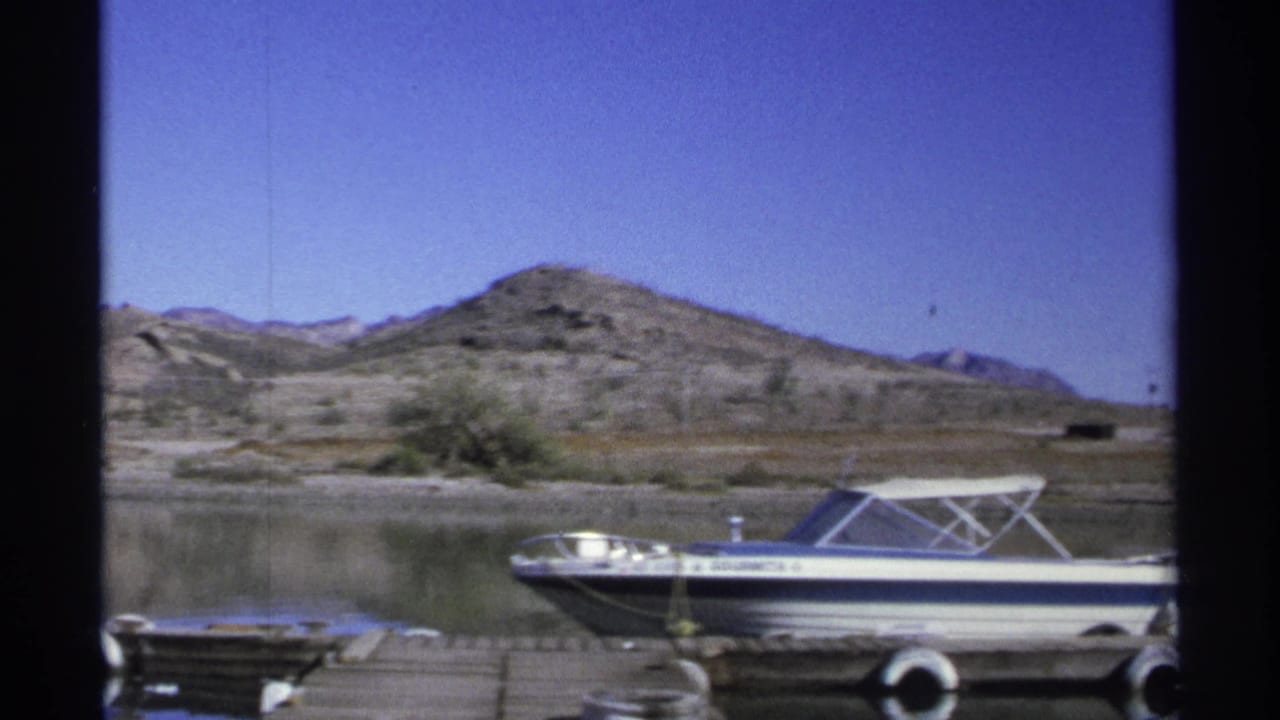 Motorboat at the dock with its name visible and hills across the water.