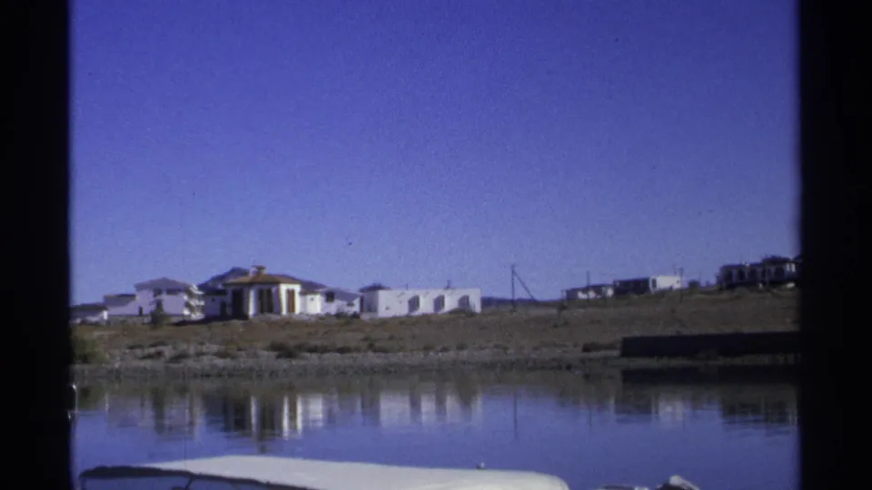 1975 8mm view of white buildings along the Guaymas waterfront with calm blue water and film frame borders.