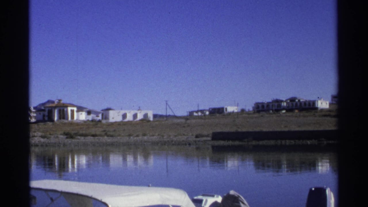 Shoreline buildings and water seen through dark film frame borders.