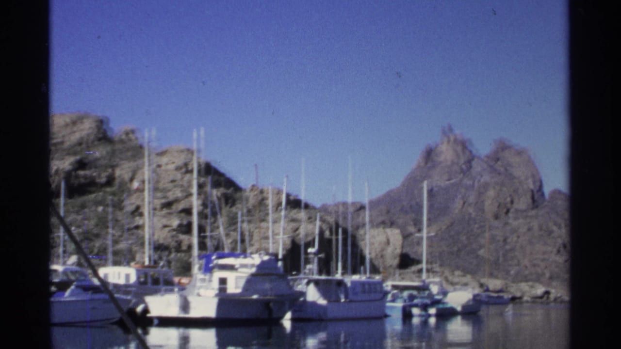 Moored boats in a marina with rocky mountains behind them.