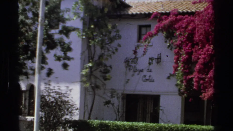 1975 Guaymas hotel exterior with white stucco walls, tiled roof, wall sign, green vines, and bright bougainvillea.