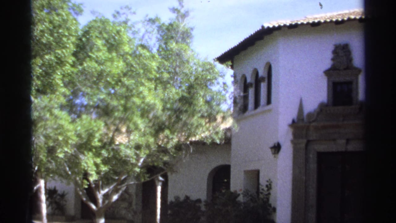 White stucco building with arched windows, tiled roof, trees, and a stone doorway.