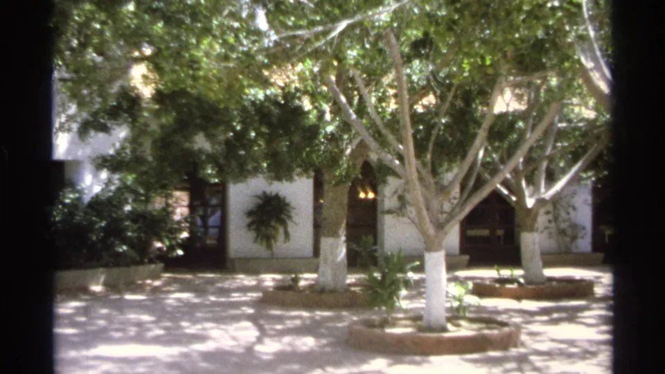 Guaymas, Mexico 1975 home-movie frame showing a bright courtyard with trees, whitewashed buildings, and a tiled fountain.