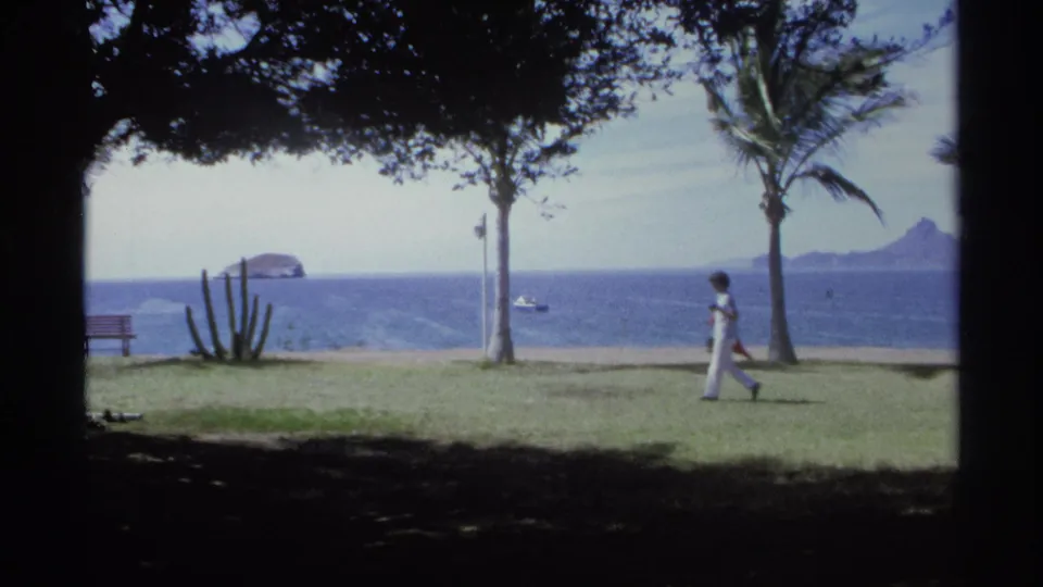 A 1975 Guaymas seaside park shot shows a person walking across the lawn between palms, with cactus, bench, boat, and islands visible.