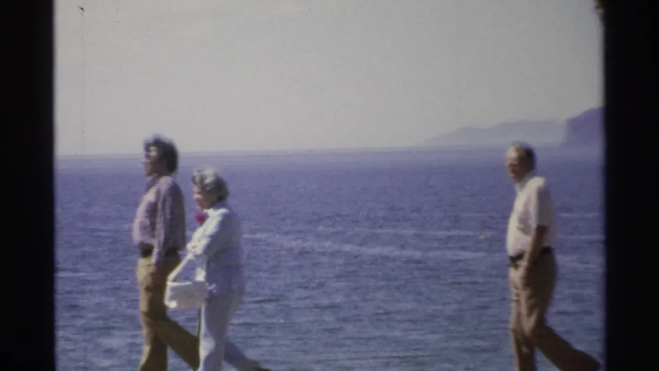Adults continue along the Guaymas waterfront, with the blue sea and distant coastal mountains visible behind them.