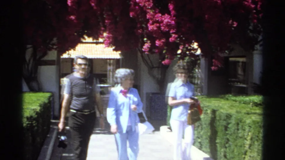 1975 Guaymas footage shows a man and two women walking through a bright courtyard bordered by hedges and bougainvillea.