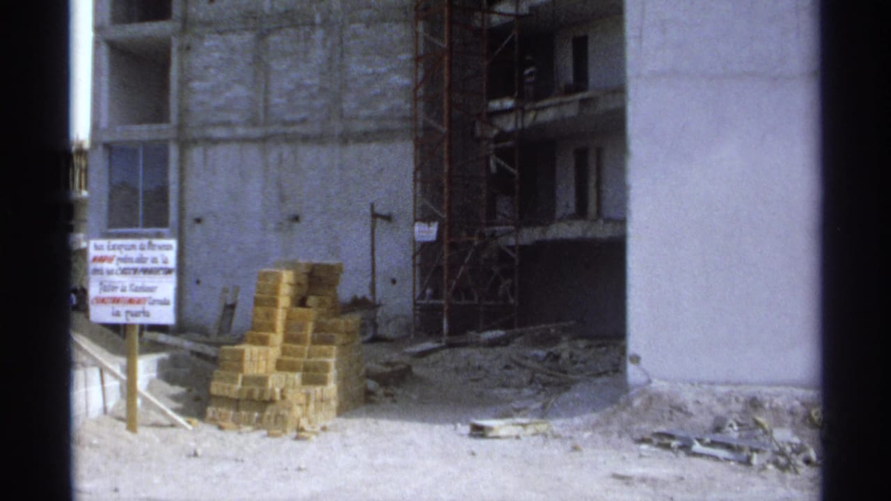 Unfinished concrete building with scaffolding, brick stacks, debris, and a Spanish sign.